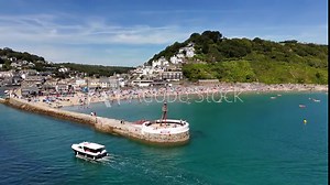 boat passing by the pier of Looe beach, people on the beach, and coastal buildings in Cornwall, UK
