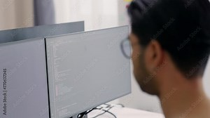 Close-up view of a male programmer's profile as he focuses intently on developing software on his computer monitor.