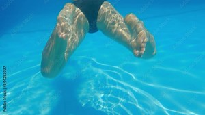 Beautiful legs of an attractive woman swimming underwater in a perfect blue pool in the rays of sunlight. Mesmerizing shot in slow motion of a girl engaged in scuba diving in a swimming pool