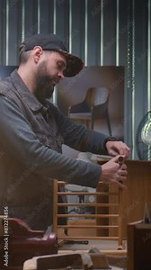 Professional craftsman, artisan assembles wooden bedside table under LED lamp using professional tool. Male carpenter works in modern workshop for making furniture. Handmade and entrepreneurship.