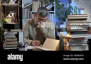 Man studying at desk surrounded by stacks of books, Focused note taking during late evening research in home library setting Stock Video Footage - Alamy