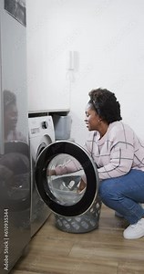 Vertical video of african american woman using washing machine and doing laundry at home