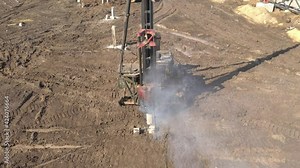 Excavation at a construction site, diesel pile driving machine with rumble and smoke drives piles deep into the ground to ensure the strength of the foundation of the future structure