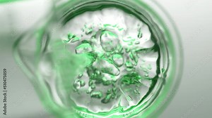 Light green liquid pouring into beaker with water from flask creates different sized bursting bubbles and ripples on its surface on light grey background | Abstract skin cleanser mixing concept