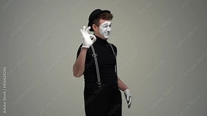 Portrait of happy male mime showing okay and thumbs-up hand gestures and winking expressing recommendation, looking at camera. Talented comic actor showing pantomime against white isolated background.