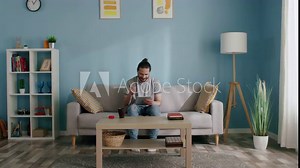 Man uses tablet computer to work, study at home, looking through needed pages, documents, happy to succeed with his task, Zoom out, Slow motion.