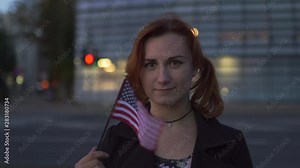 Redhead woman portrait holding USA American Flag with glass building in the background - Traveler and explorer