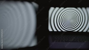 Two computer screens in a dark room displaying a hypnotic spiral pattern. Stock Video