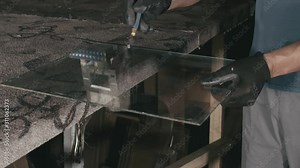 Forge. Smithy. Glass cutting and processing for fireplace doors. Circular glass cutter. Worker cut glass with glass cutting diamond. Polish an angle grinder with an abrasive circular disk nozzle.
