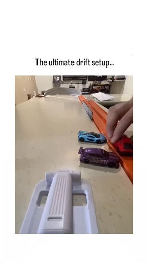ViralSnap on Instagram: "- This 8-second video is pure toy-car satisfaction. A hand positions a red Hot Wheels car at the top of an orange track launcher, sending it flying down the ramp. The car hits a sharp curve and executes a flawless 180-degree drift across the smooth countertop. It slides perfectly into a "parking space" right next to a blue and a purple car, coming to a dead stop in a neat line. The process repeats with rapid-fire precision, showing multiple red cars hitting the exact sam