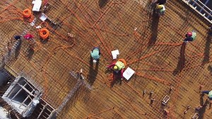 Group of workers, electricians and builders are installing hoses and reinforcement bars on the last floor of building construction before concreting, aerial view, drone flying and rotating up.