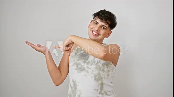 Cheerful young man, proudly showing off in a sleeveless t-shirt, joyfully pointing and presenting with his hand. the amazed lad stands confidently against a clean white isolated background.