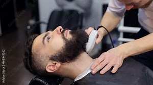 Male Barber shaves the beard of a brutal man using an electric shaver in a modern barbershop. Close-up.