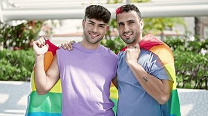 Two men couple hugging each other holding homosexual flag at park