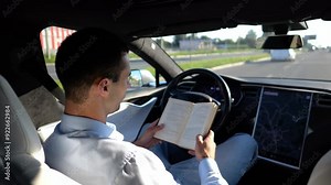 Male businessperson reading book during riding on electrical vehicle with autopilot at urban road. Successful businessman improving his knowledge while riding an autonomous self driving electric car