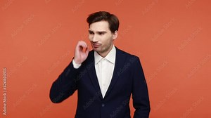 Hmm, need to think. Frustrated confused bearded guy in official suit scratching head, holding chin, contemplates how to solve problem, has doubts. Indoor studio shot isolated on orange background.