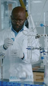 Medium vertical of African American scientist in white coat, gloves, glasses standing in chemistry laboratory, carefully drawing transparent liquid into test tube using squeeze bulb pipette Stock Video