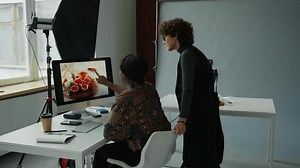 Female photographer showing reference image on computer screen to food stylist getting ready for shoot day in studio