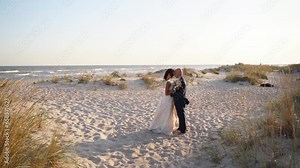 Just married couple hugging, expressing feelings at sandy coast at sunset. Young bride, groom enjoying summer evening on honeymoon at seaside. Pretty woman and man posing at the romantic photoshoot.