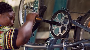 Close-up shot of athletic female cyclist meticulously examining and correcting damages on bicycle pedal and crank arm. Dedicated black woman ensuring the functioning of bike chain rings.