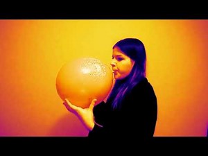 Girl blows up a large birthday balloon balloon until it pops