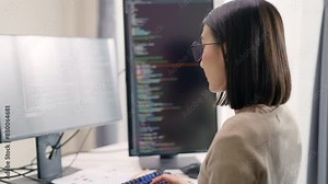 An Asian female programmer, deeply focused on her coding tasks, is working on multiple monitors in a modern office, Ideal for illustrating themes related to information technology, web development.