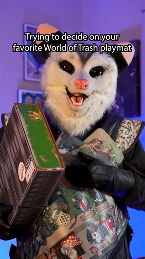 Don’t let them be alone. Get all 4 during Gen Con at booth 670. This is the World of Trash – Trash Day Manager’s Special set, and yes… I absolutely caved when I saw the opossum playmat! These mats are thick, high quality, and you can toss them in the washing machine (because I get messy when I try to eat and game, and I have regrets). Each set comes with all 4 mats, a pin, a coin, sticker sheets, and this glorious card box that is dumpster-styled. Honestly? It’s the most beautiful trash I’ve eve