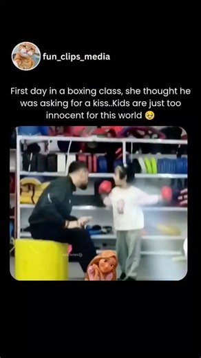 Fun Clips Media on Instagram: "A heartwarming viral video captures a young girl's first day in boxing class, where innocent misunderstanding leads to an adorable moment. A little girl, around 5-6 years old, wears oversized red boxing gloves and practices basic punches in a gym under her coach's guidance. The coach, seated on a stool, extends his fist for a standard fist bump. The child misinterprets it as a request for a kiss—she leans in puckering her lips to kiss his hand. The surprised coach 