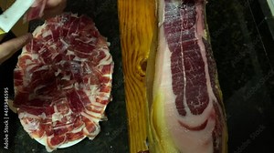 A front leg of Serrano Iberian ham also known as Spanish Pata Negra mounted on a wooden stand with a butcher cutting slices-Dan