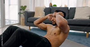Exercise, workout and fitness with a man doing sit ups in the living room of his home for health and wellness. Motivation, training and healthy with a male athlete exercising his body in a house
