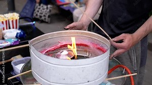 Seller Makes Cotton Candy, a Machine for Making Cotton Candy on the Street. Burning burner in a container melts sugar. Children's party. Selling street sweets. Close up. Slow motion.