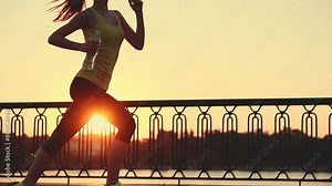 Slow motion: running woman. Runner is jogging in sunny bright light. Female fitness model training outside in the city on a quay. Sport lifestyle. Filmed at 240 fps.