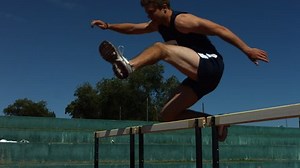 Track athlete jumps over hurdle, slow motion