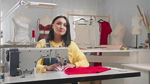 The seamstress is embroidering on her sewing machine in her small, but beautiful, atelier. As she looks at the camera, she smiles. She has started her own small business. Medium shot. Slow motion.
