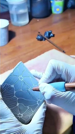 Gloved hands carving floral ceramic pattern with precision