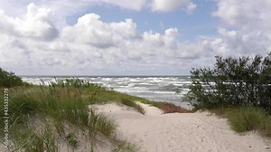 Typical Baltic sea coast landscape view in Lithuania. Blue sky with white clouds, foamy waves in the sea and sand dunes partially overgrown with sedge grass .