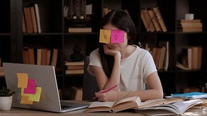 Tired brunette student has two colored stickers on her eyes. Exam and test period at college. Student studies and reviews the learned material. Concept of studies, students, college