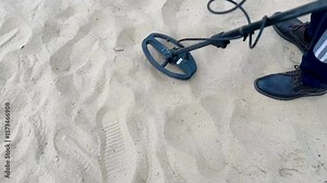 Person scanning beach sand with metal detector in search of hidden treasures.