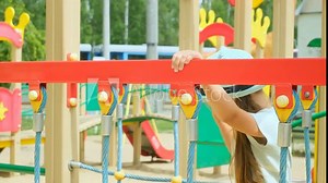 Little girl is playing on a colorful playground slide. The slide is made of metal and has a blue, red, and green design. The girl is climbing up the slide and he is enjoying herself