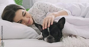 Woman in bed with dog. Caucasian girl, French bulldog, dog sleeping together. Wide shot.