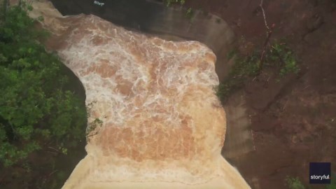 Aerial footage shows floodwaters gush over 120-year-old dam