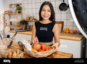 An attractive Asian female food blogger is cooking in front of the camera, recording a video of herself making healthy food in her home kitchen Stock Photo - Alamy