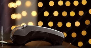 Woman's hand with hand watches using terminal for payment, non-cash transaction, side view. Non-cash payment concept. Pos-terminal on table on black background with yellow light spots.