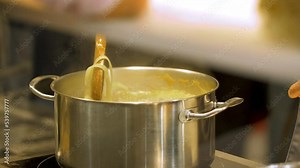 Boiling pasta in a pot full of hot boiling water. Spaghetti is being stirred by a chef with a wooden spoon to not stick together. Liquid is steaming. Traditional homemade Italian cuisine.