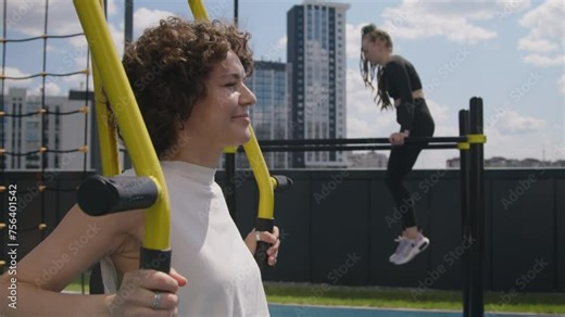 Side chest up footage of sporty Caucasian 40yo woman training on outdoor push pull chair fitness equipment during arm workout at rooftop gym
