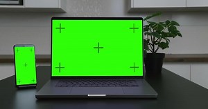 A laptop and smartphone side by side on a desk, both displaying green screens, emphasizing digital devices, technology, and workspace setup.