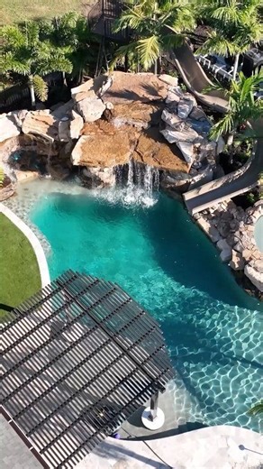 Welcome to resort living at home! We custom-designed and built this incredible rock waterfall pool in Land O’ Lakes, Florida. Highlights include a towering natural rock waterfall, slide, elevated spa, metal pergola, sun shelf, and a huge walk-in cave. #insanepools #lucaslagoons #pool #waterslide | Lucas Lagoons