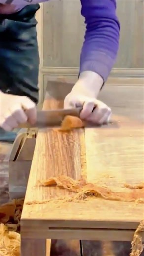 smoothing a large wooden table surface using a manual scraper tool to create thin wood shavings now