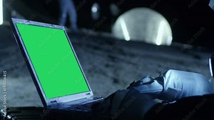 Astronaut on the Alien Planet Works on a Mock-up Green Screen Laptop. In the Background Her Crew Member and Living Station. Colonization Concept. Shot on RED EPIC-W 8K Helium Cinema Camera.