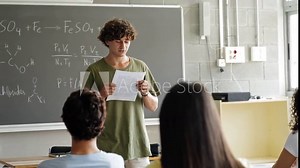 College student presenting a project reading a presentation to classmates and teacher at High School classroom